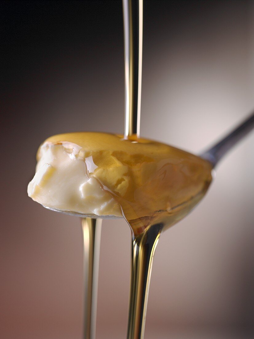 Vanillecreme auf einem Löffel mit Honig übergiessen