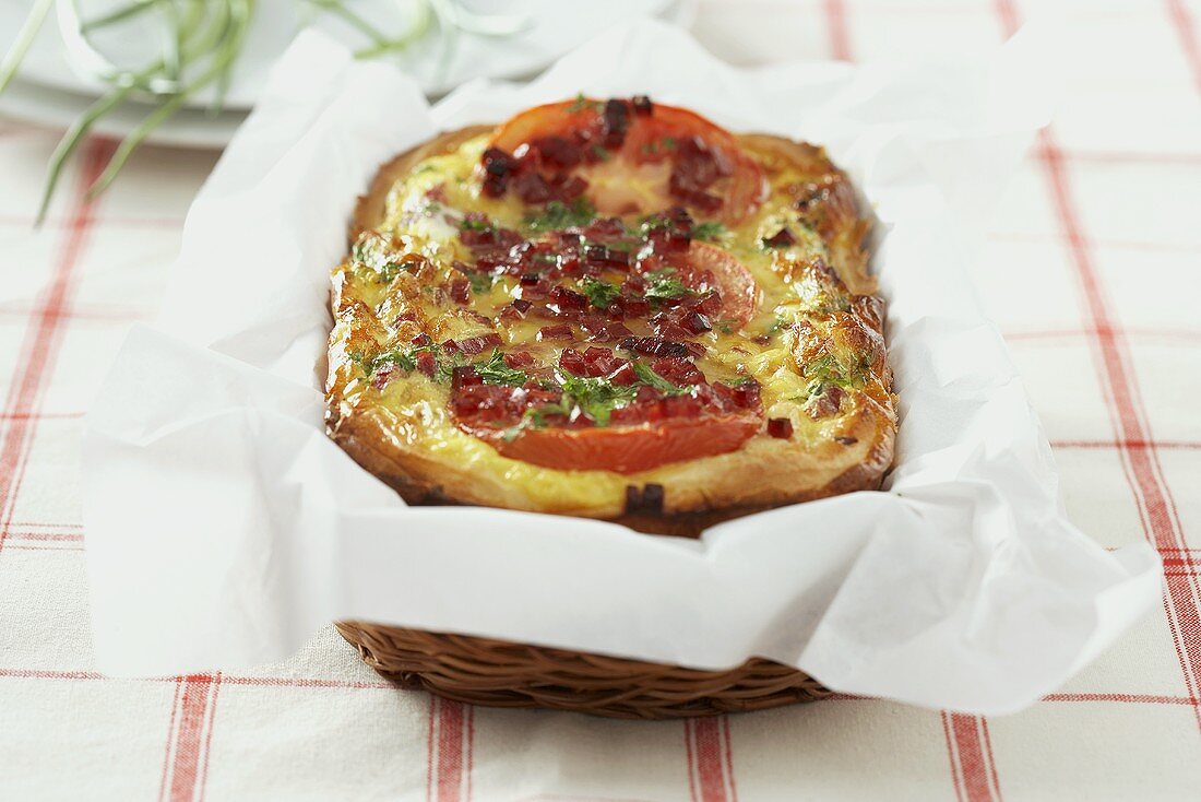 Ham, tomato and cheese quiche on paper in a small basket