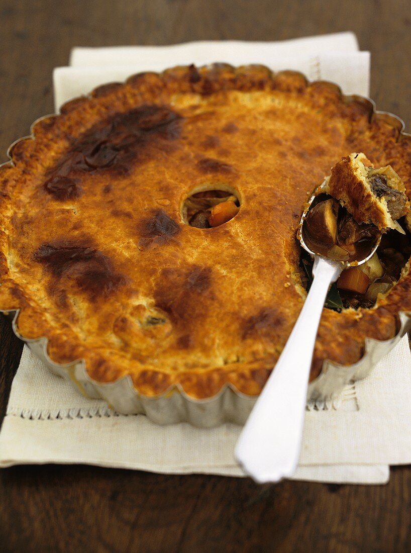 Beef and vegetable pie in a pie dish with a spoon