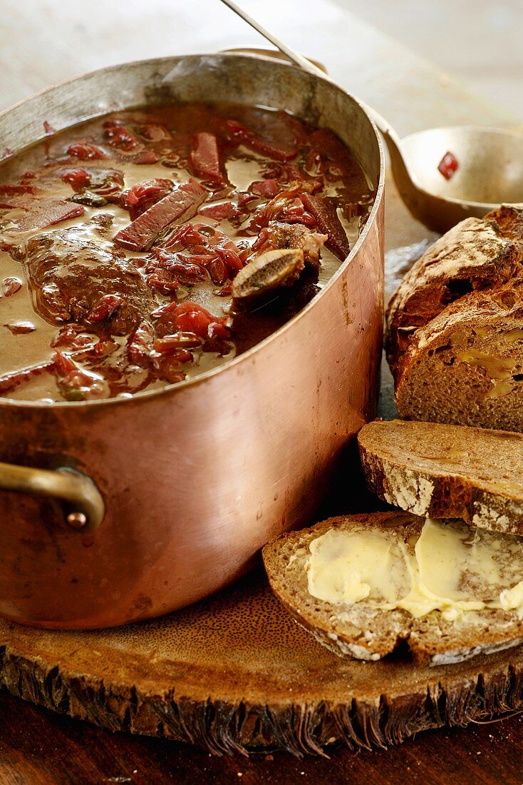 Beetroot soup with beef in a copper pot, slices of bread