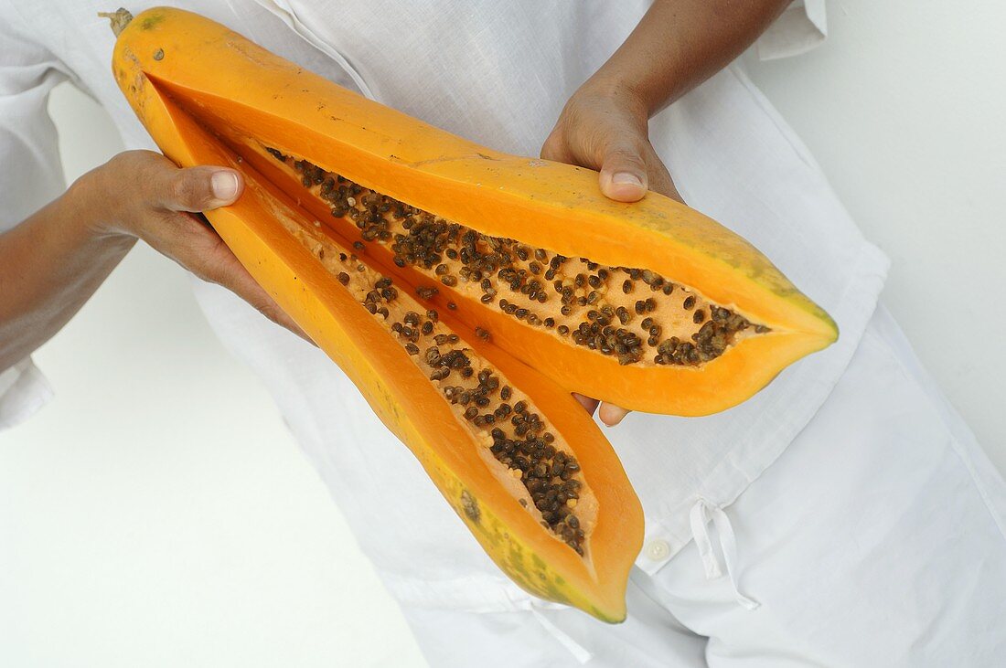 Hände halten eine aufgeschnittene Papaya in den Händen