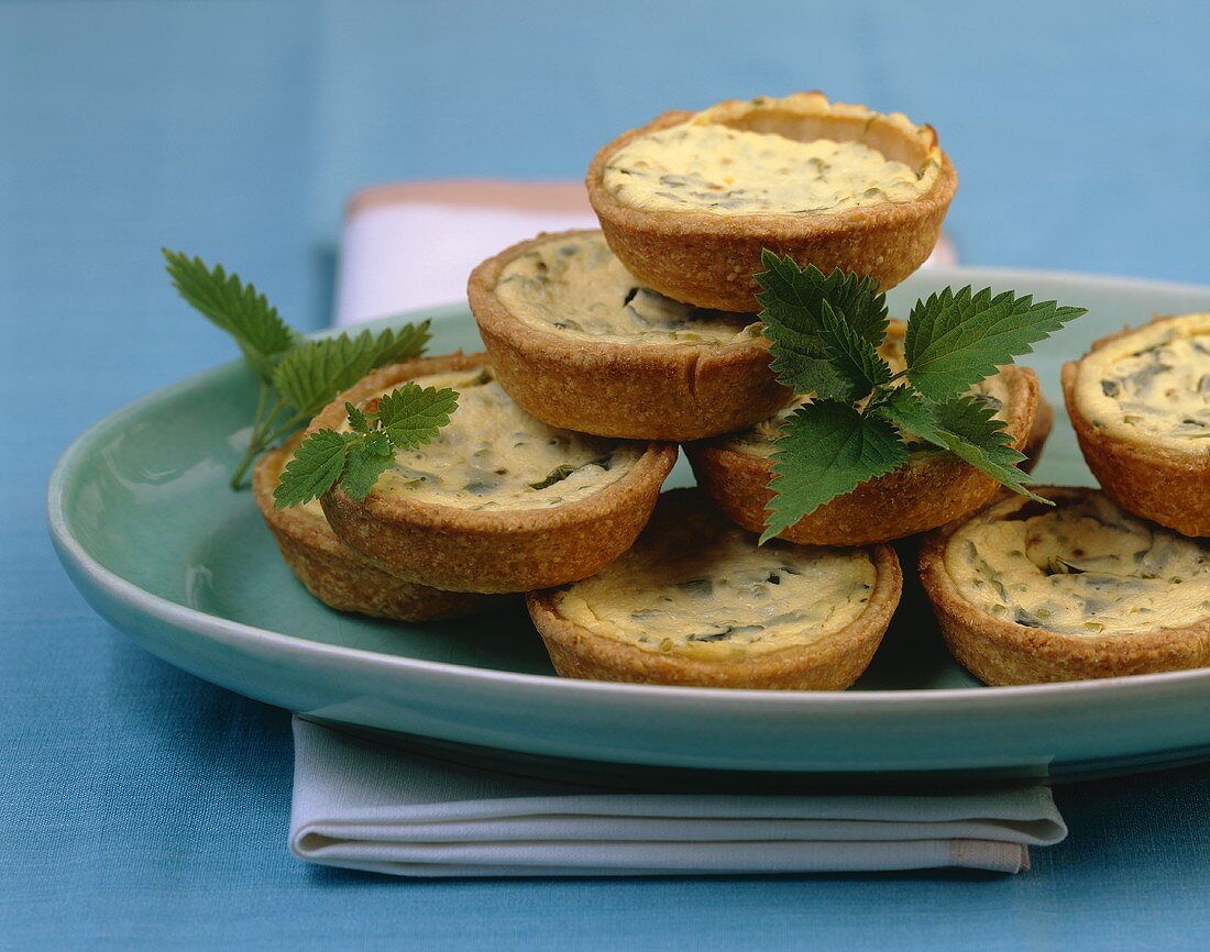 Small sour cream & nettle quiches, in a pile on a platter