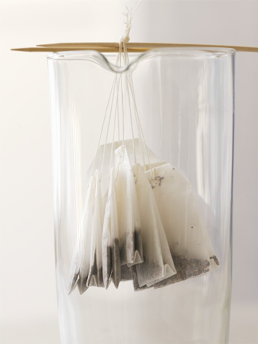 Several tea bags hanging on wooden sticks in a glass beaker
