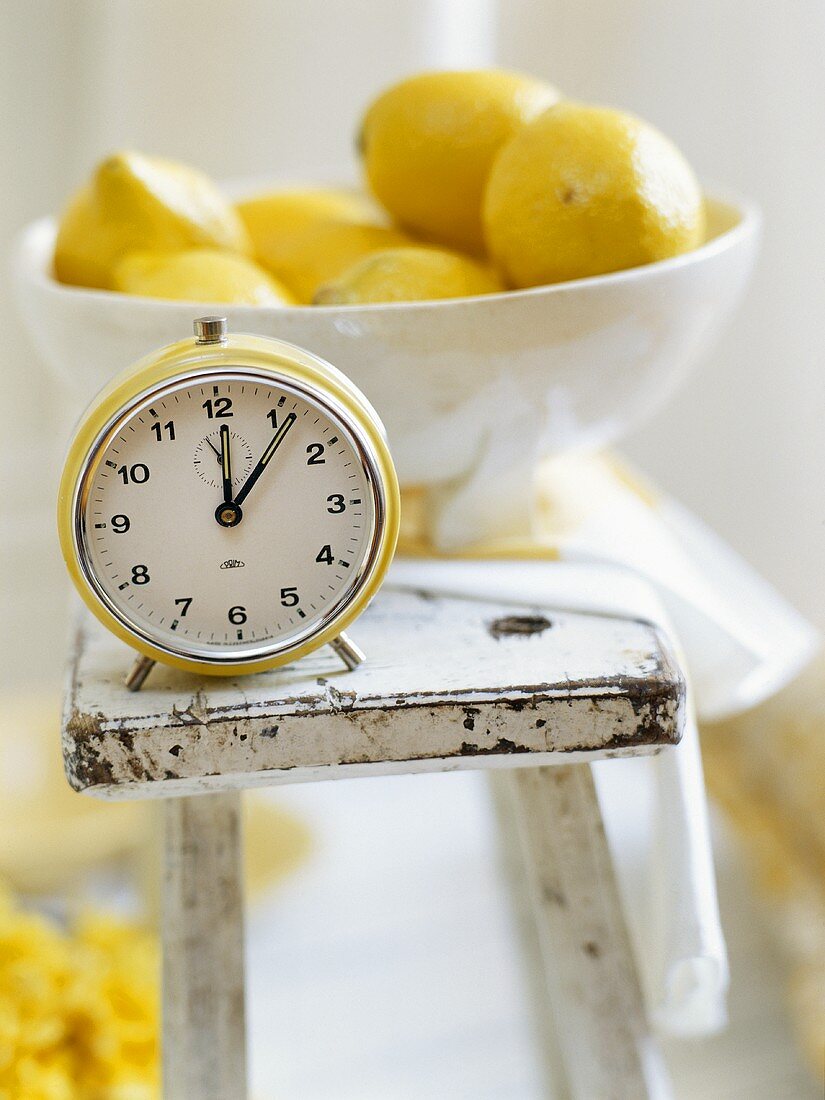 A bowl of lemons and an alarm clock on a stool