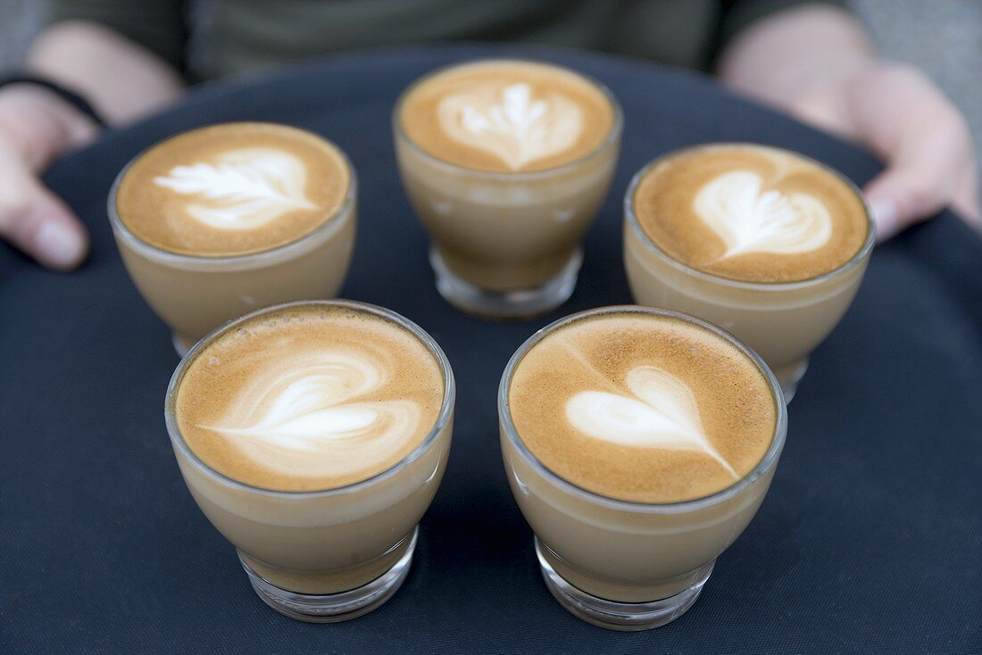 Frau trägt ein Tablett mit Cappuccino mit Michschaumherzen