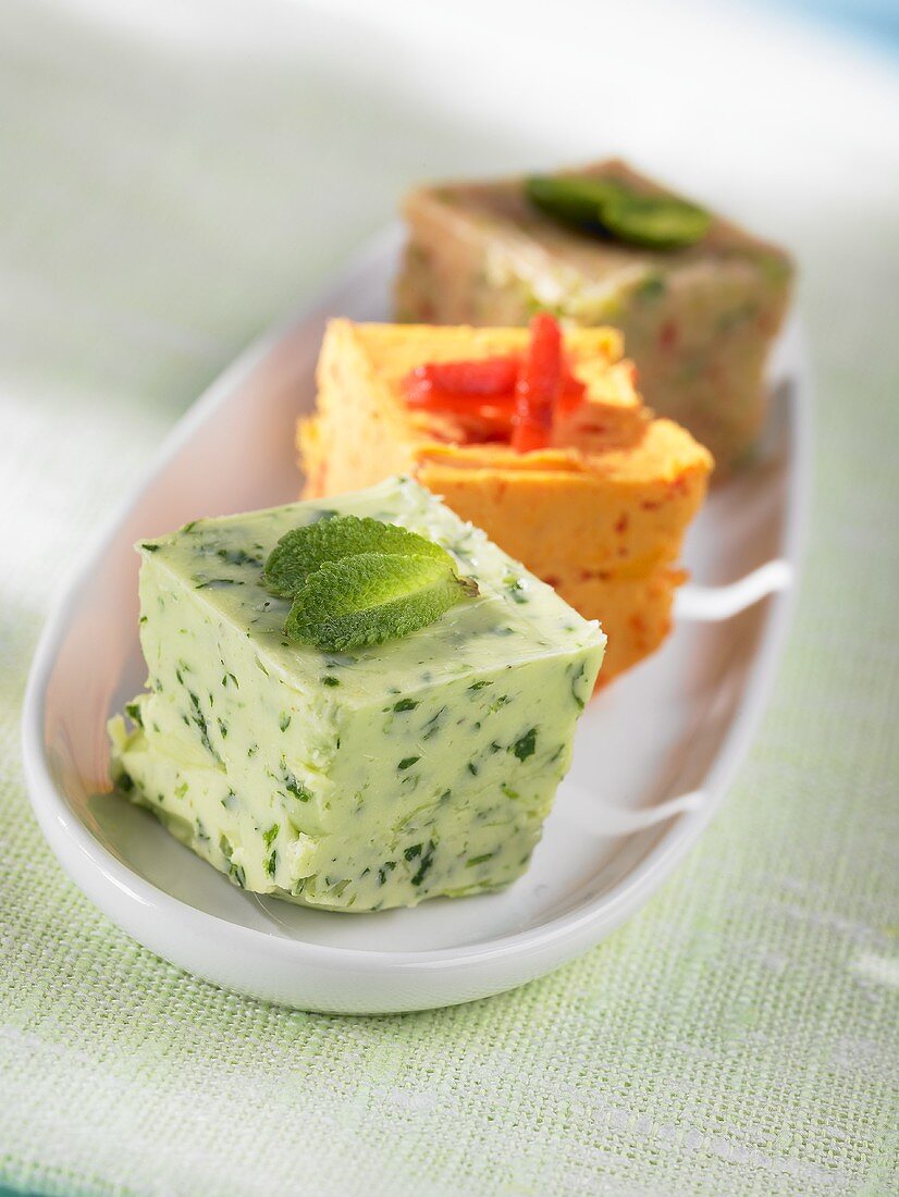 Three cubes of herb and spice butter in a small dish