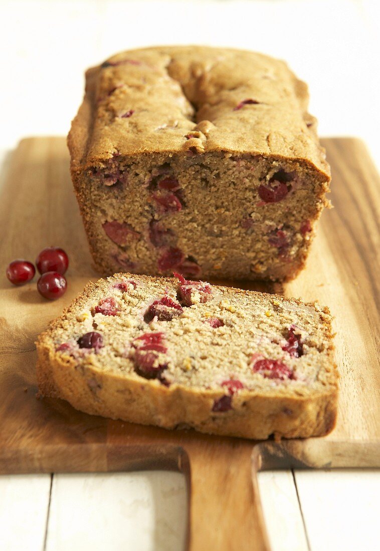 Cranberry bread, partly sliced on a wooden board
