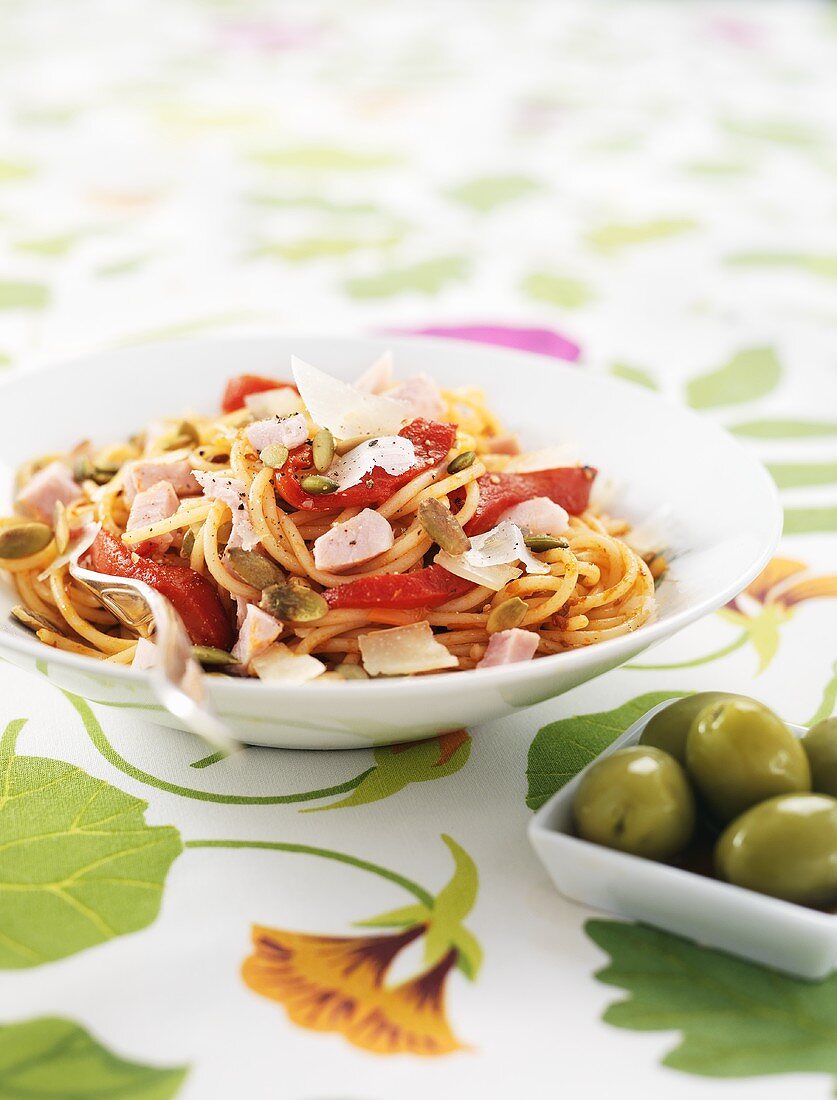 Spaghetti with ham, peppers, pumpkin seeds and olives