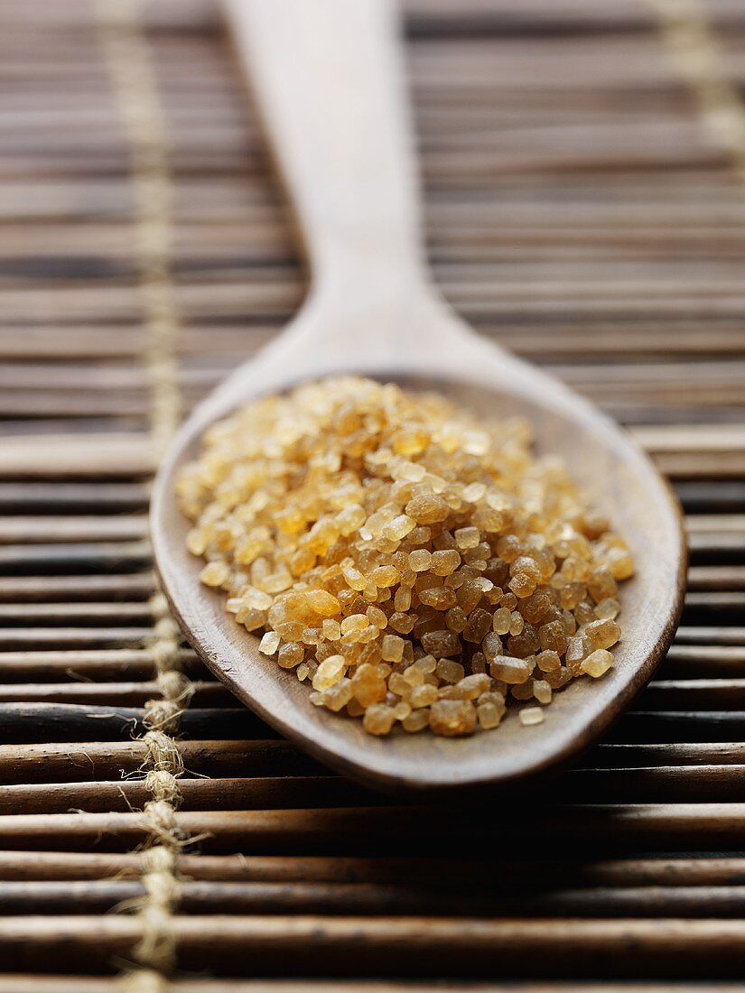 Raw cane sugar in a wooden spoon on a bamboo mat