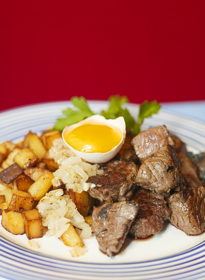 Cubes of beef steak with fried potatoes and an egg yolk