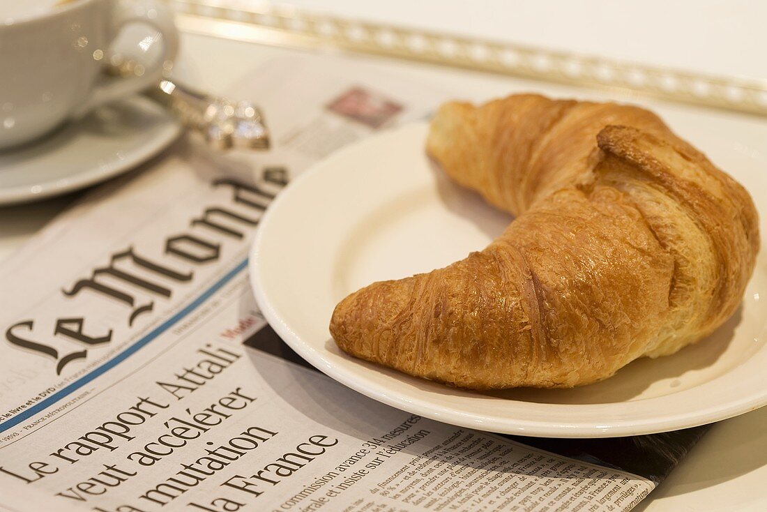 Croissant auf französischer Zeitung mit einem Milchkaffee