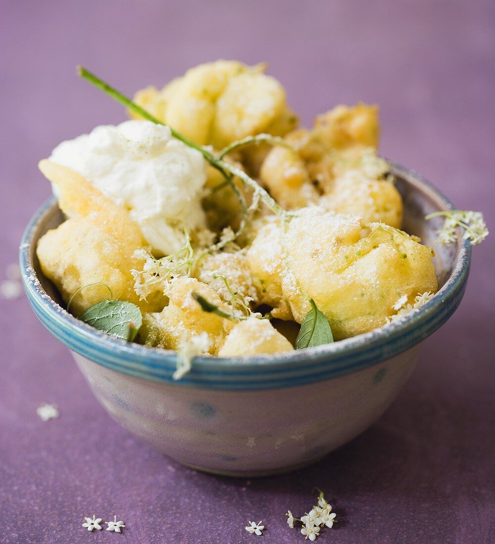 Elderflower fritters with icing sugar in a ceramic bowl