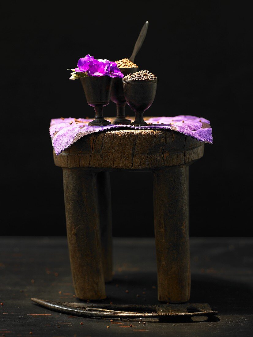 Gewürze und Blumen in Bechern auf einem Holzschemel