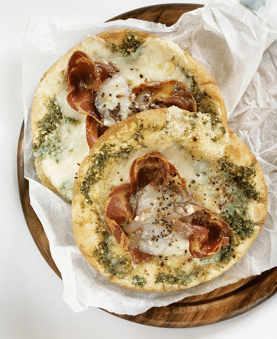 Two pizzas topped with coppa, cheese and pesto