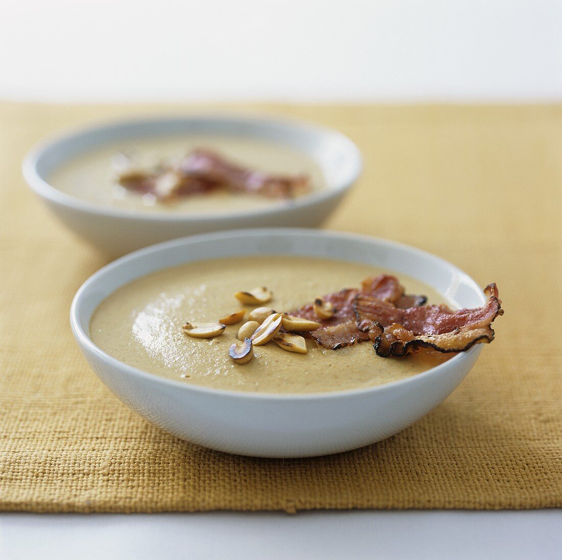 Two plates of peanut soup with fried bacon