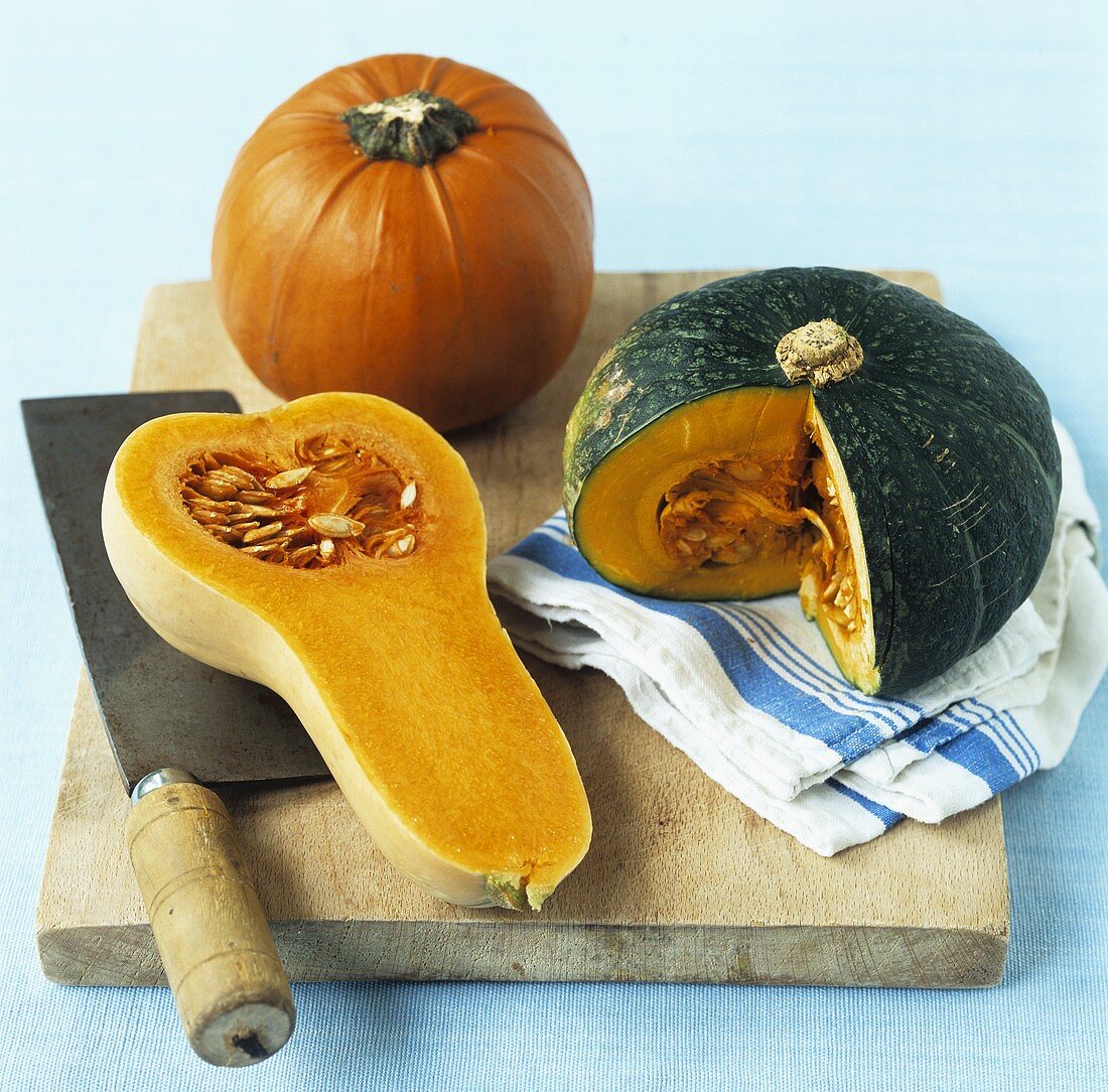 Various pumpkins & squashes on wooden board with cleaver