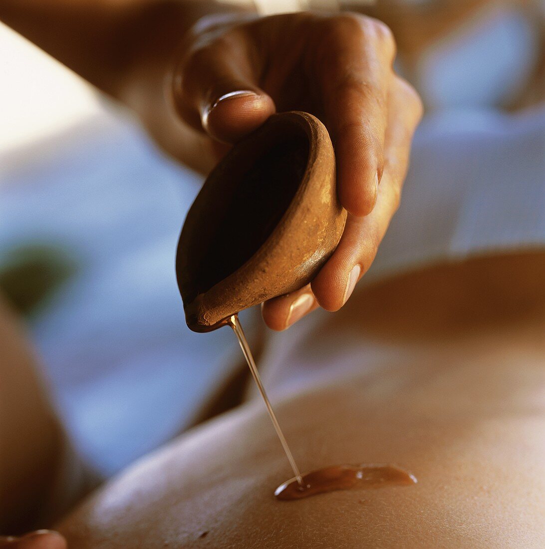 Mann giesst Massageöl aus einer Tonschale auf einen Rücken