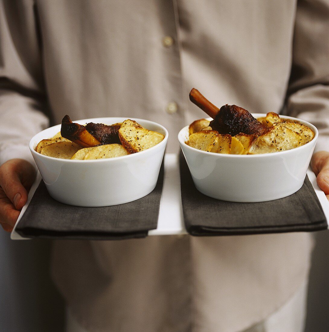 Man carrying tray with two dishes of lamb stew with potatoes