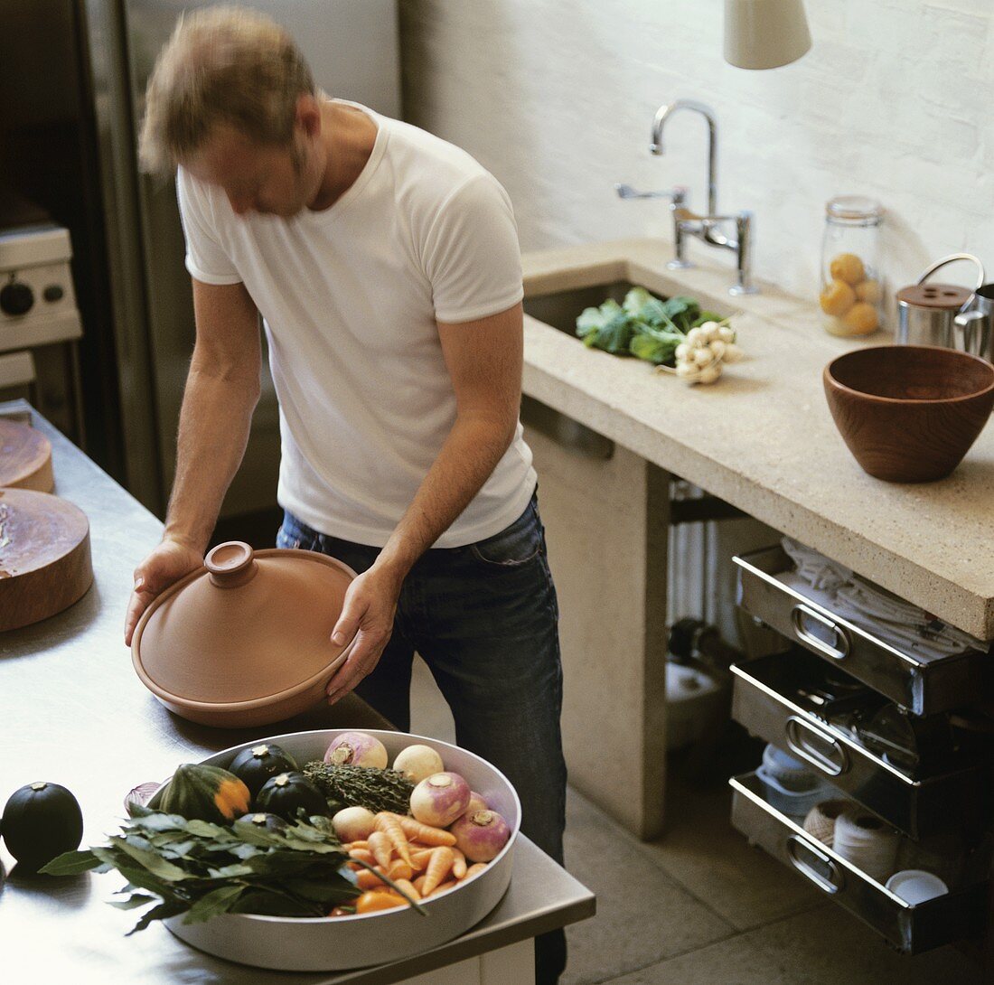 Mann bereitet Gemüse-Tajine in der Küche vor