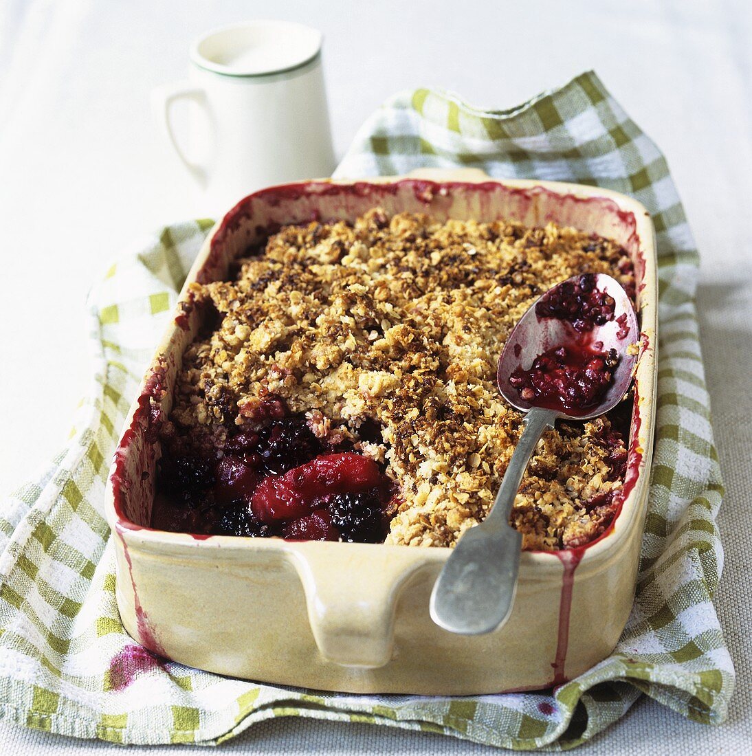 Apfel-Brombeer-Crumble in einer Auflaufform mit Sahnekännchen