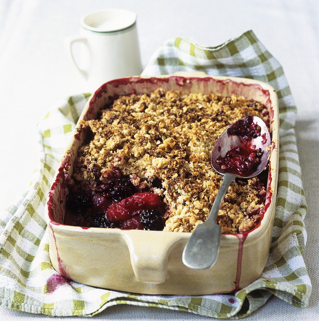 Apple and blackberry crumble in a baking dish, jug of cream
