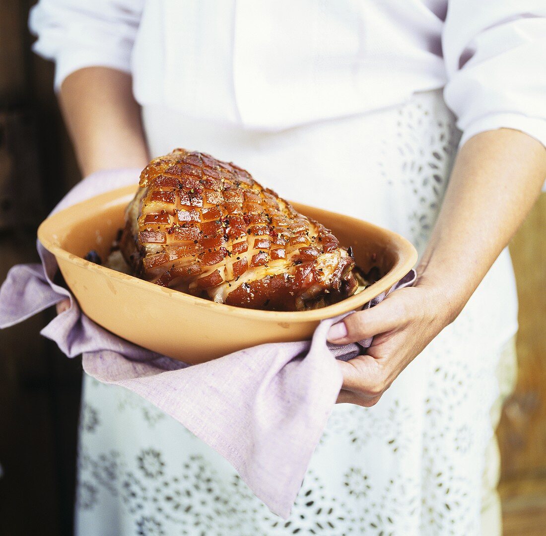 Woman holding roast ham in terracotta pot