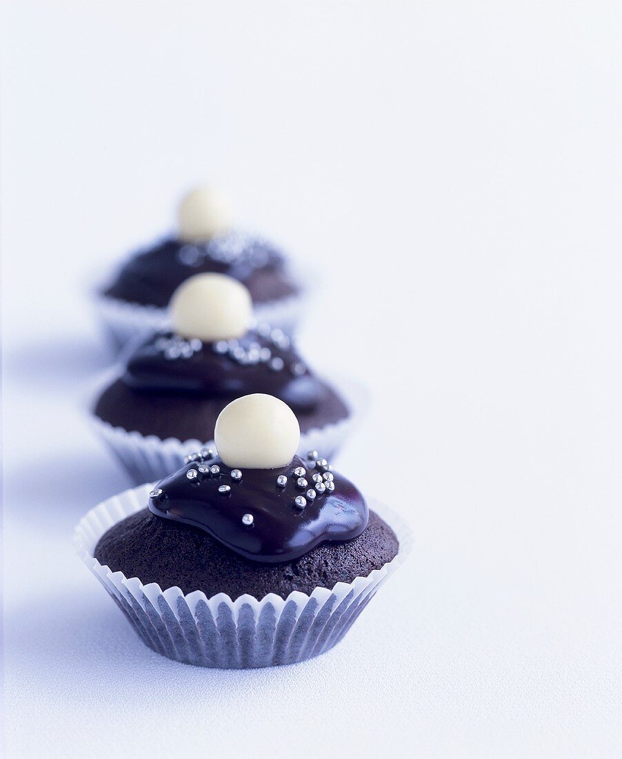 Three iced chocolate cupcakes with silver dragées