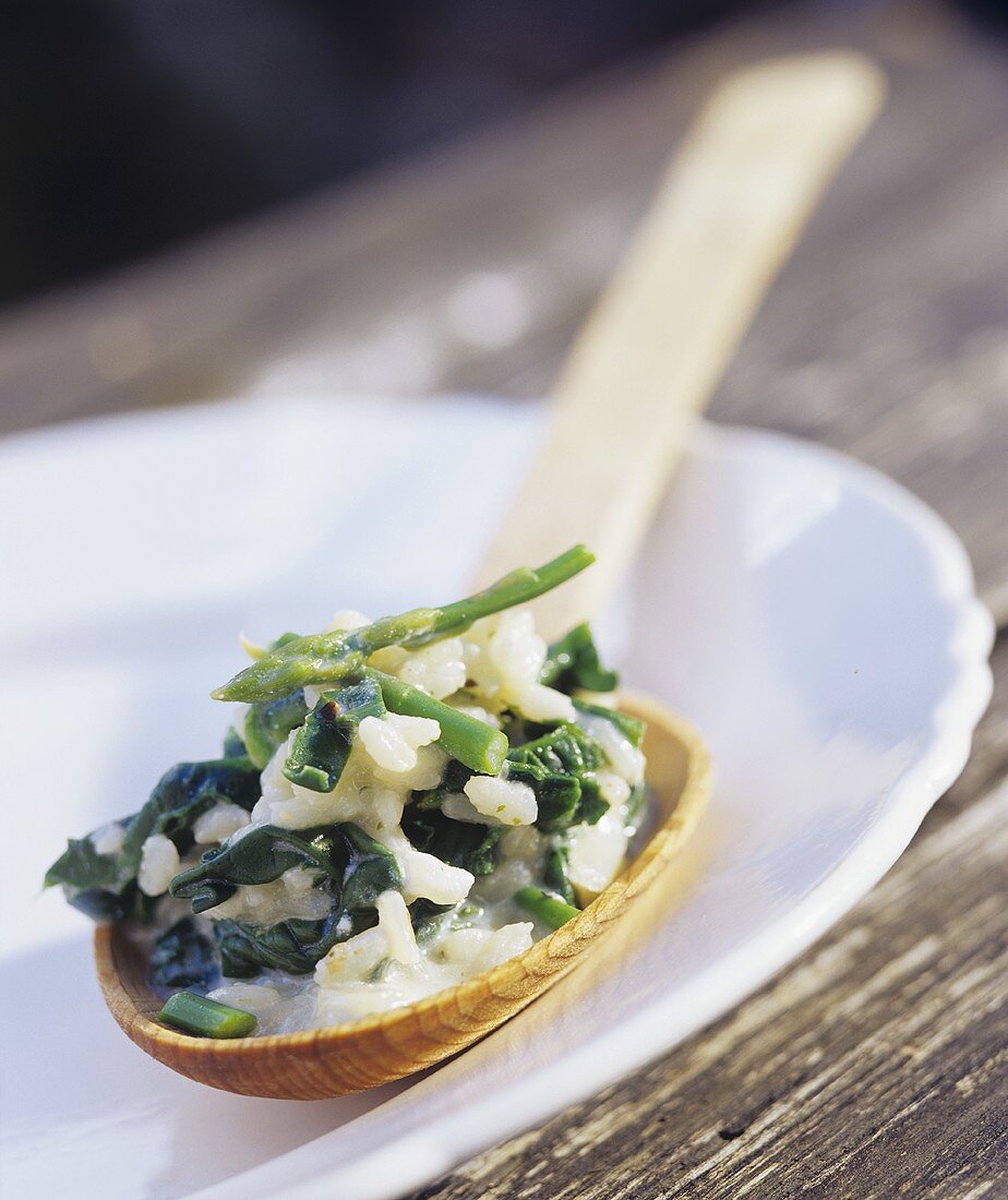 Spinach risotto with asparagus on a wooden spoon