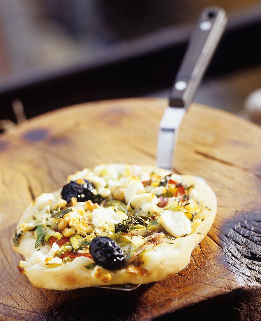 Mini-pizza topped with leeks, feta, herbs, anchovies, olives