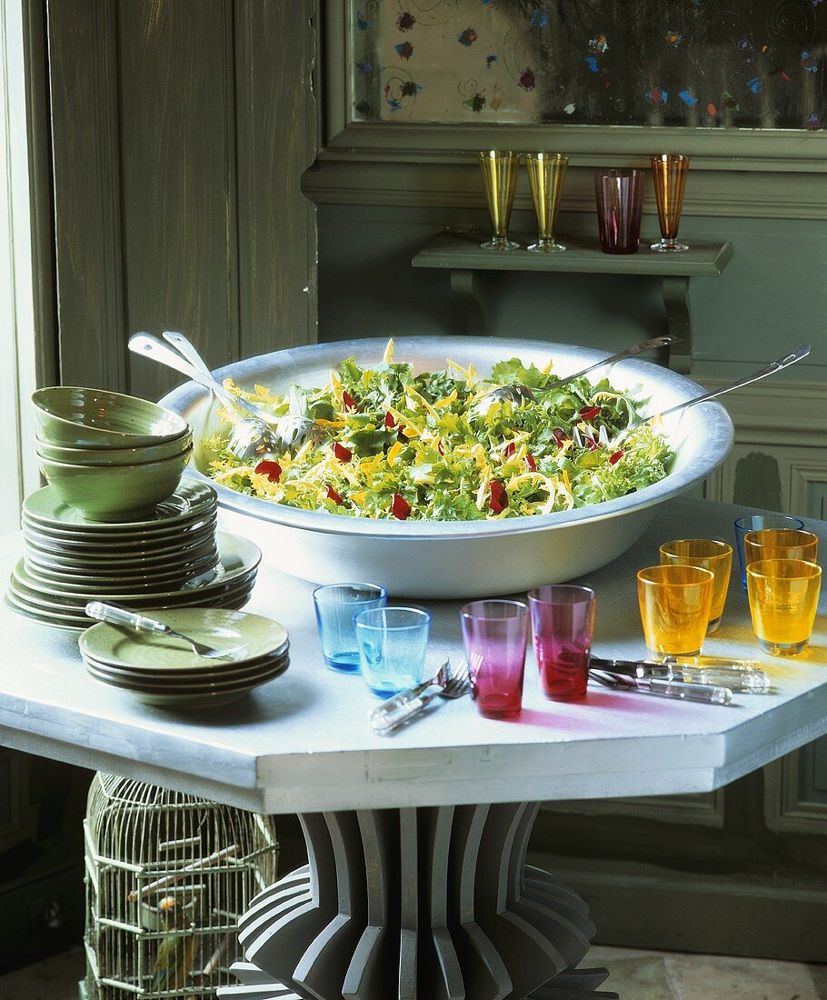 Large dish of mixed salad leaves, crockery and glasses