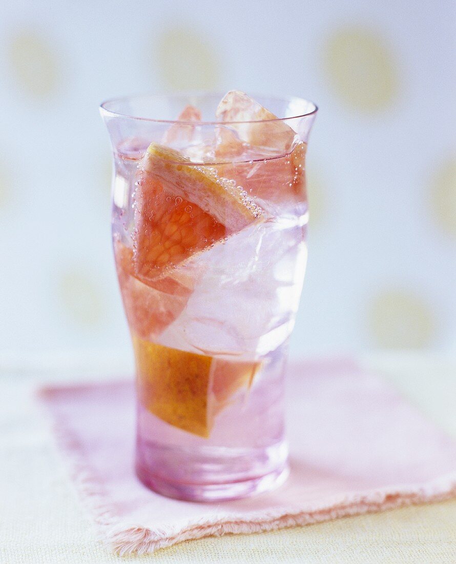 A glass of grapefruit drink with ice cubes