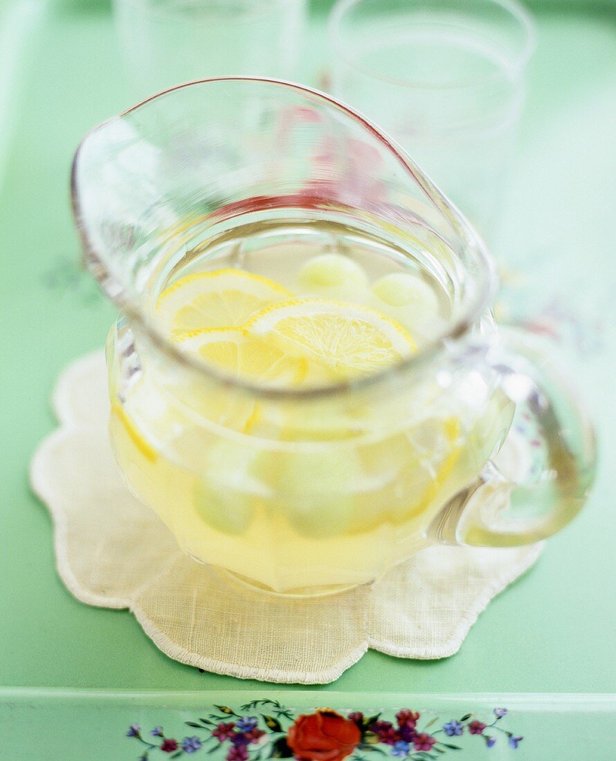 A glass jug of lemon punch with melon balls