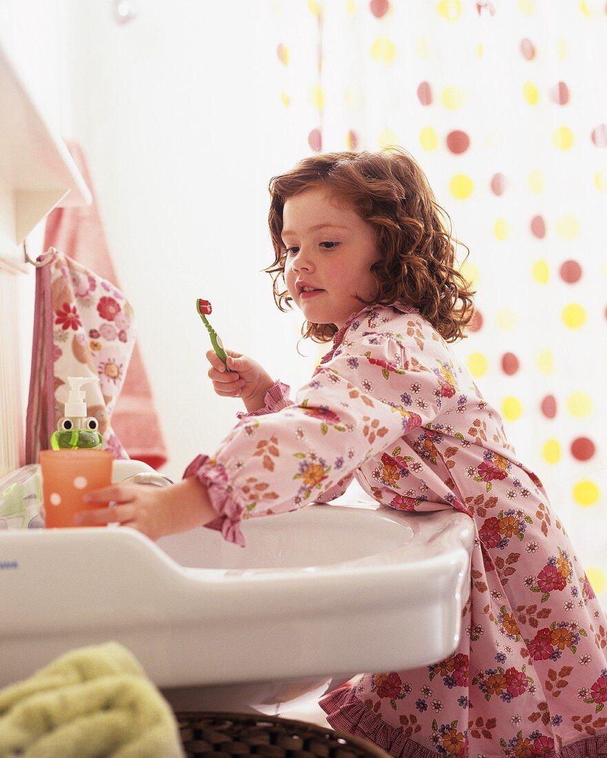 Little girl in bathrobe at wash basin with toothbrush