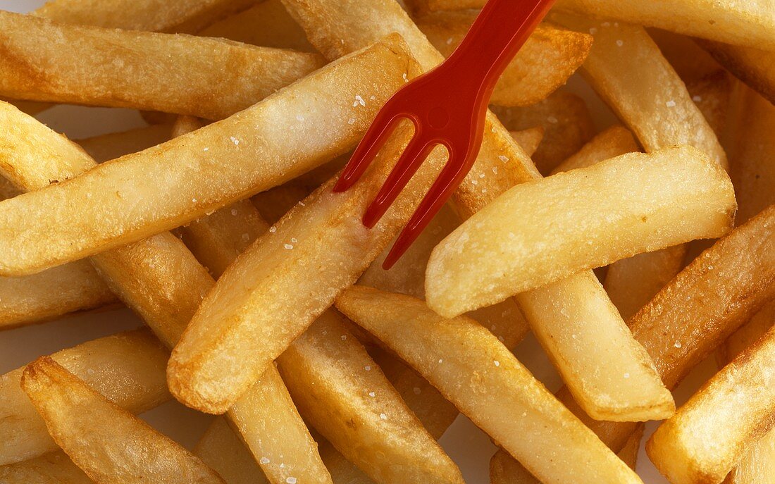 Pommes frites mit roter Plastikgabel, bildfüllend