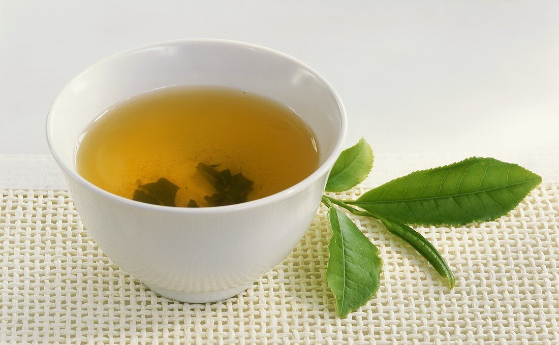Grüner Tee in Teeschale und frische Teeblätter
