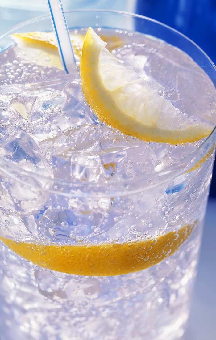 A glass of water with ice cubes, lemon and straw