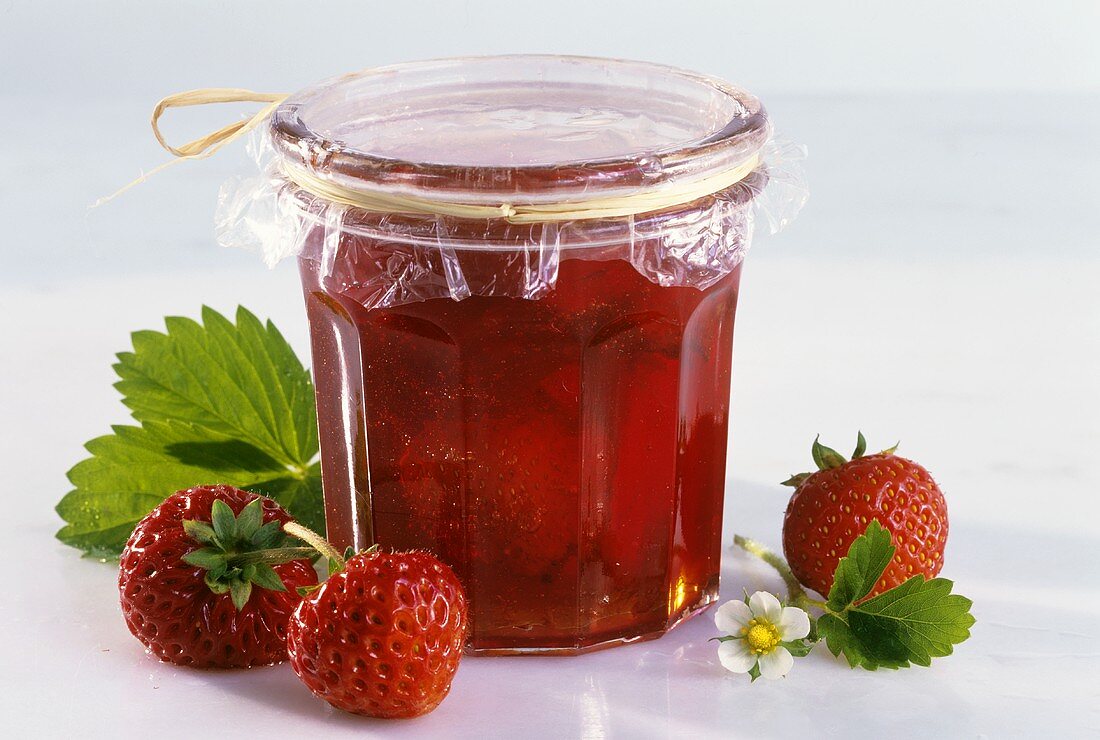A jar of strawberry jam with fresh strawberries