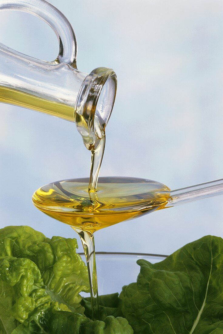 Olive oil running over spoon into a bowl of lettuce