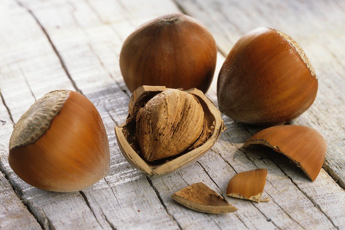 Hazelnuts, three unshelled and one shelled on wooden background