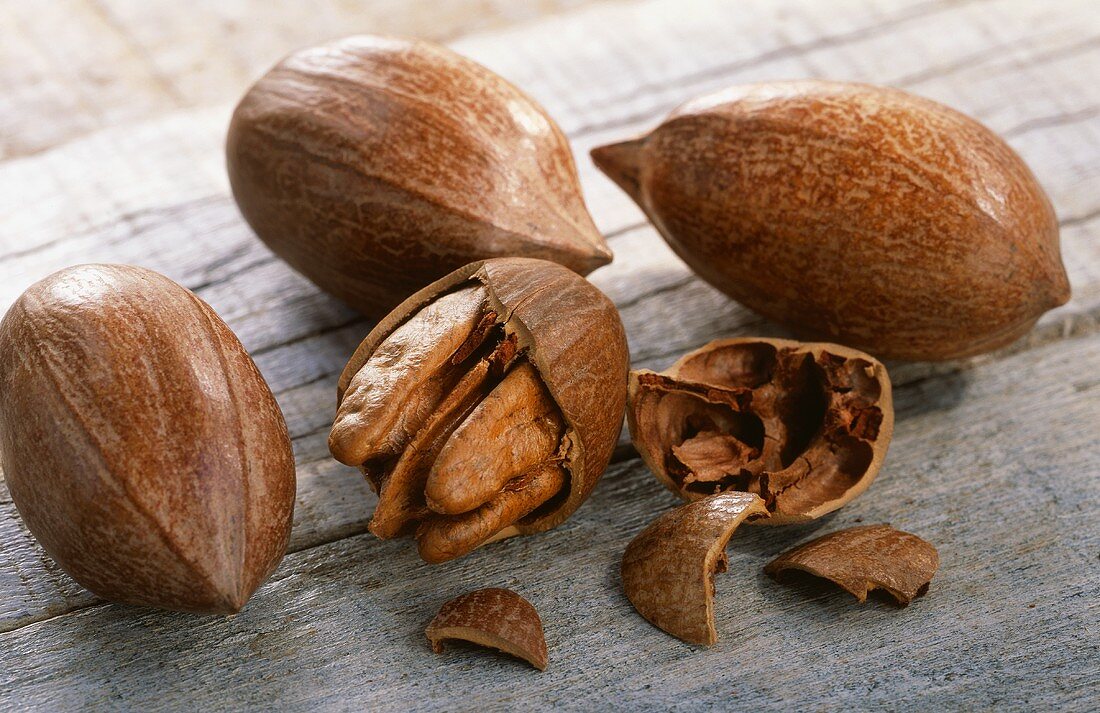 Three unshelled and one shelled pecan on wooden background