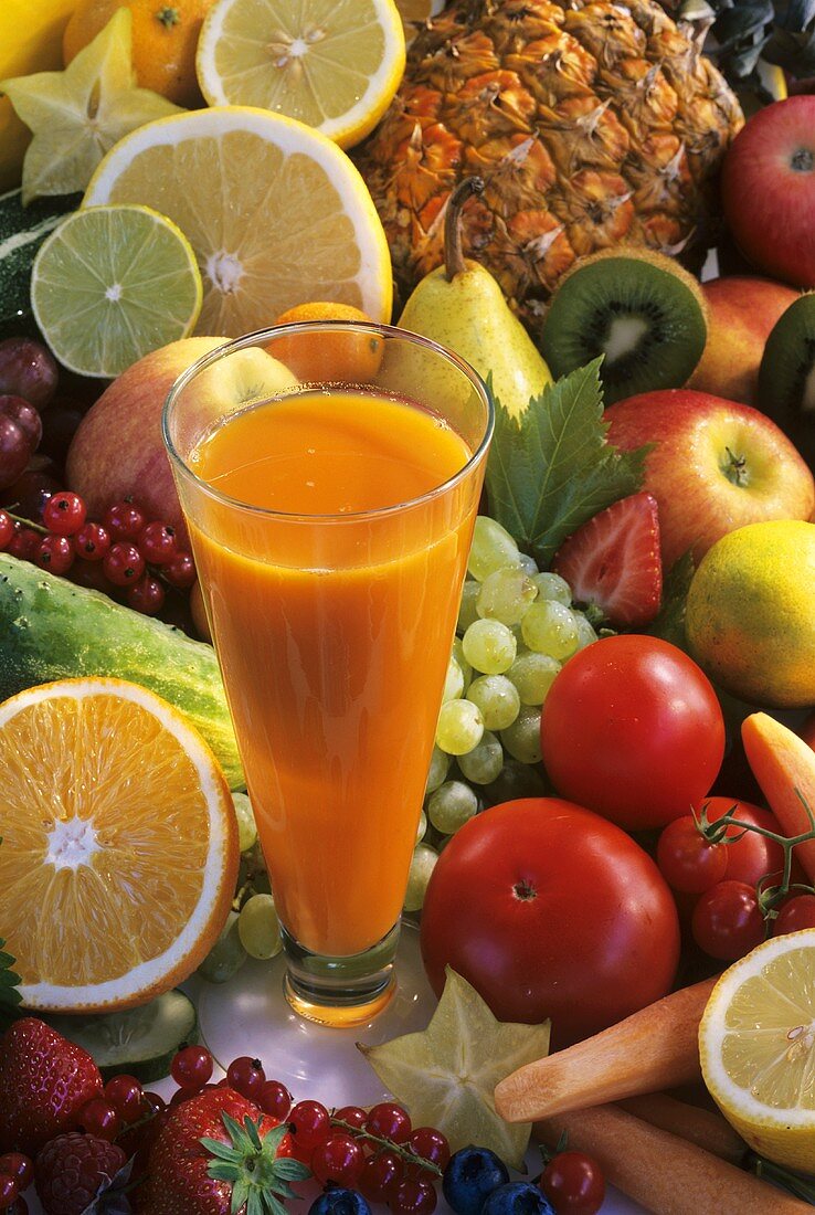 Glass of carrot and papaya juice surrounded by fruit and vegetables