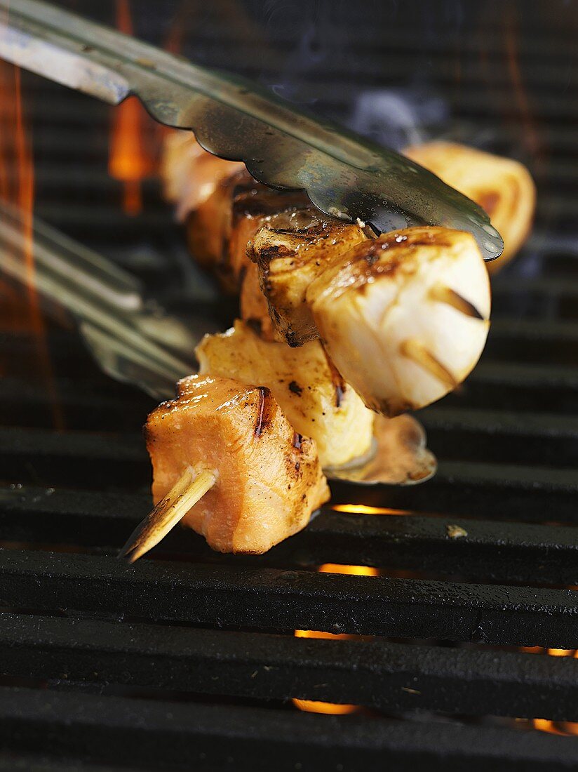 Fish kebabs being turned with tongs