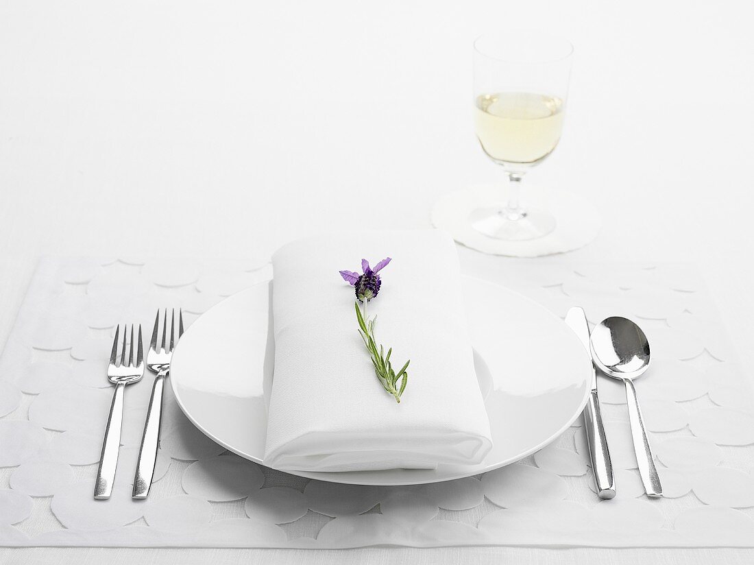 A place setting with a white napkin and a sprig of lavender