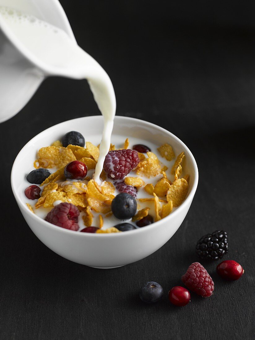 Milk being poured onto cornflakes and berries