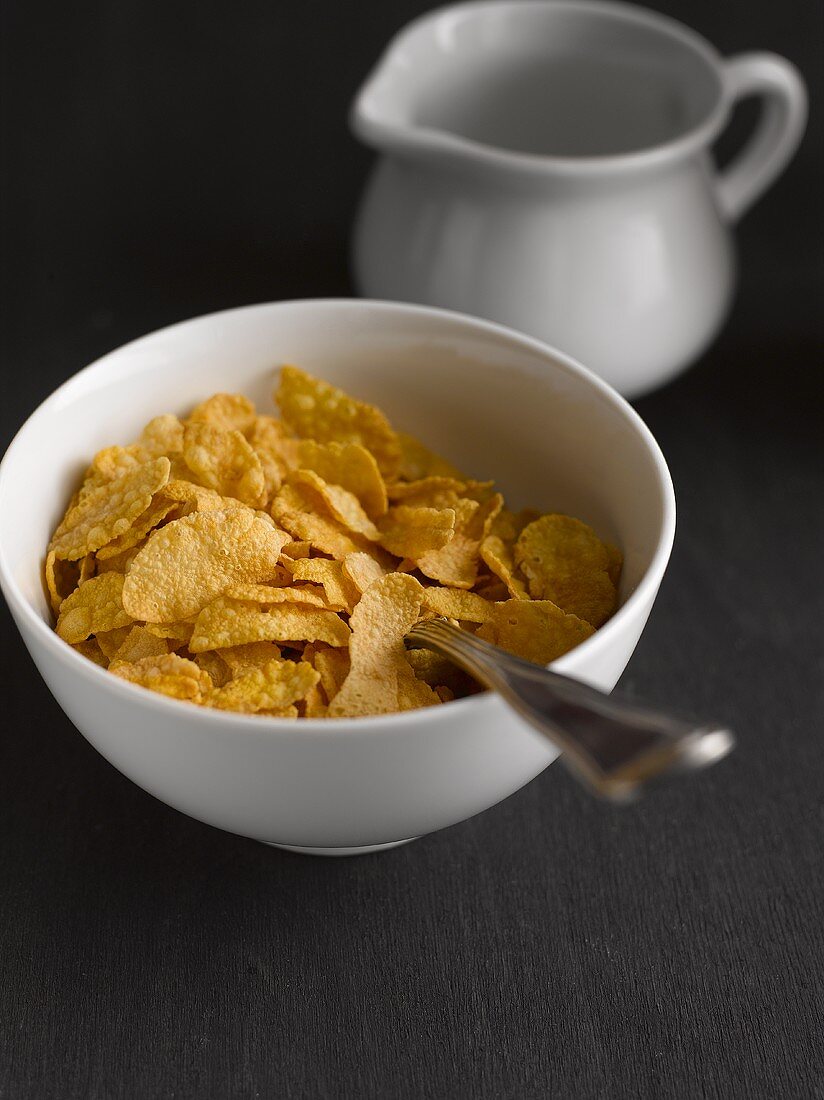 Cornflakes in a bowl in front of a jug of milk