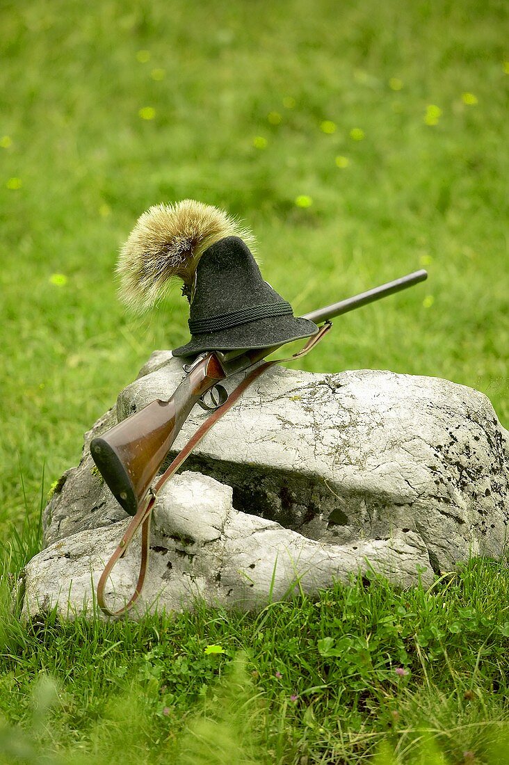 Jagdgewehr und Hut mit Gamsbart auf einem Stein in der Natur