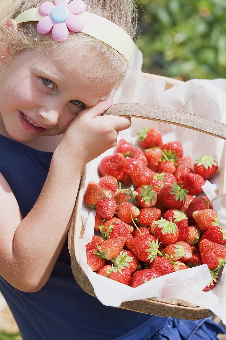 A girl in a garden holding a basket of strawberries