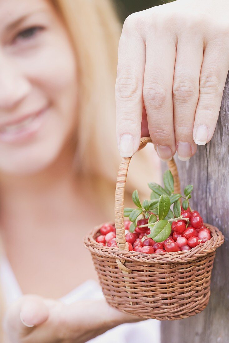 A woman holding a little basket of lingon berries