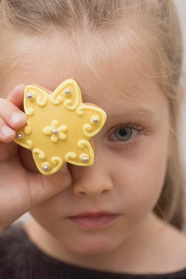 A little girl holding holding a biscuit in front of her eye