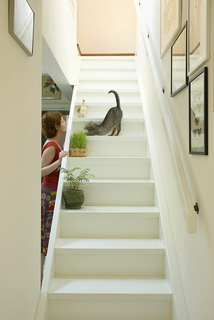 A woman playing with a cat on a flight of white wooden stairs